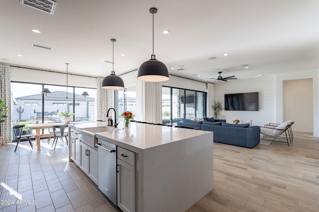 kitchen featuring ceiling fan, pendant lighting, a kitchen island with sink, dishwasher, and light wood-type flooring