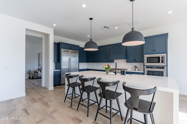 kitchen featuring a kitchen breakfast bar, a large island with sink, built in appliances, and blue cabinets