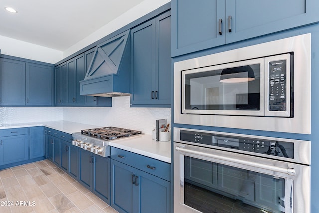 kitchen featuring blue cabinets, tasteful backsplash, stainless steel appliances, light wood-type flooring, and premium range hood