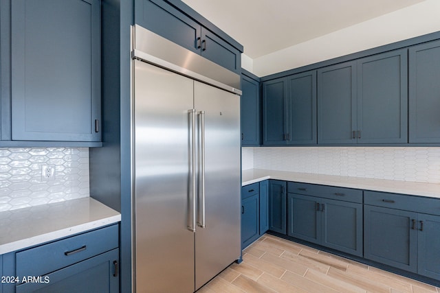 kitchen with stainless steel built in fridge, blue cabinetry, light hardwood / wood-style flooring, and tasteful backsplash