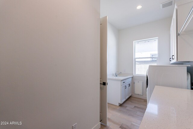 clothes washing area featuring washer / clothes dryer, cabinets, light wood-type flooring, and sink