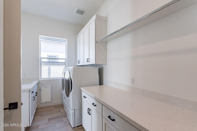 laundry room featuring cabinets, sink, light hardwood / wood-style floors, and washing machine and clothes dryer