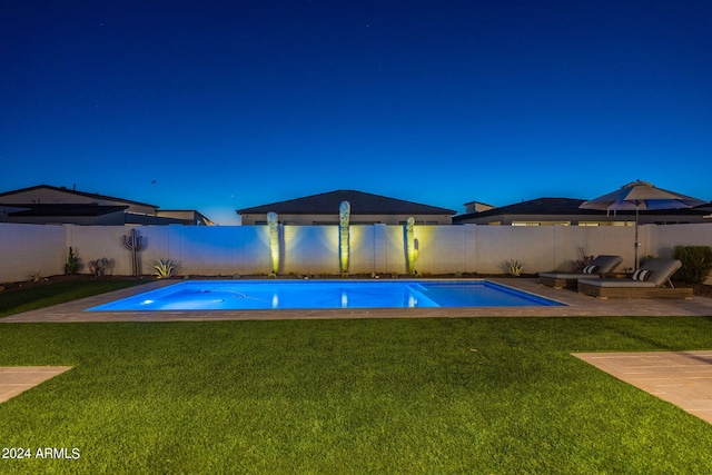 pool at night featuring a yard and a patio area