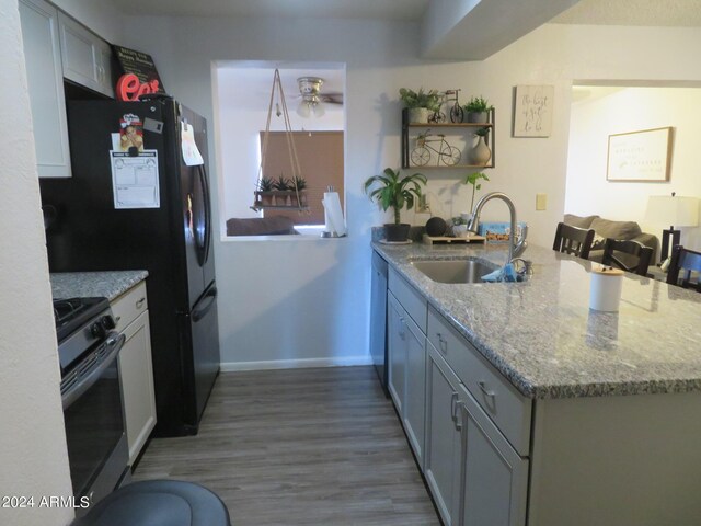 kitchen featuring appliances with stainless steel finishes, kitchen peninsula, light stone countertops, hardwood / wood-style flooring, and sink