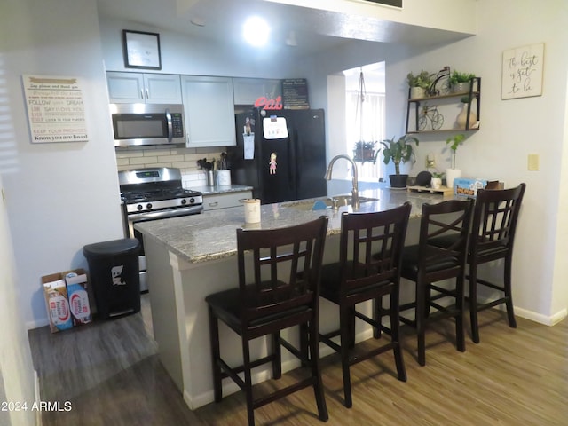 kitchen featuring tasteful backsplash, hardwood / wood-style flooring, stainless steel appliances, a breakfast bar, and light stone countertops