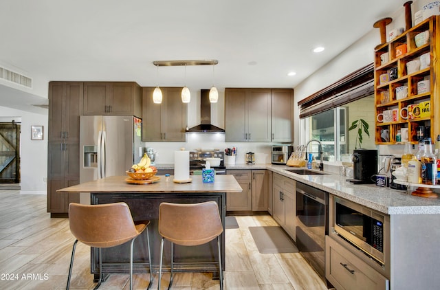 kitchen featuring a kitchen island, appliances with stainless steel finishes, pendant lighting, wall chimney exhaust hood, and sink