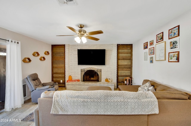 living room with ceiling fan, hardwood / wood-style flooring, and a brick fireplace