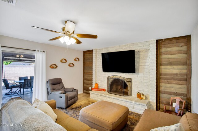 living room featuring ceiling fan, wood walls, and a fireplace