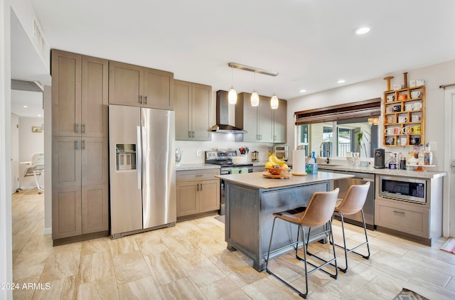 kitchen featuring wall chimney range hood, a breakfast bar area, stainless steel appliances, a center island, and decorative light fixtures