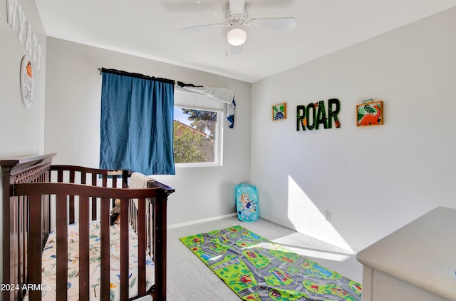 carpeted bedroom with ceiling fan and a nursery area