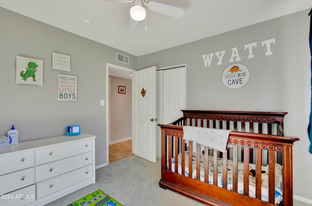 bedroom with a closet, light colored carpet, a crib, and ceiling fan