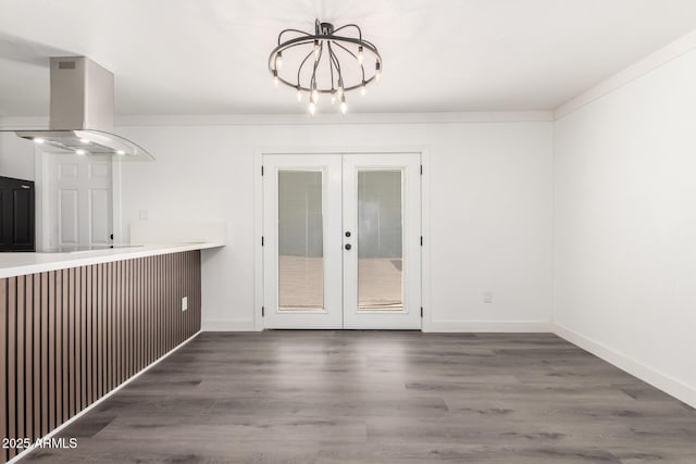 unfurnished dining area featuring french doors, baseboards, wood finished floors, and a notable chandelier