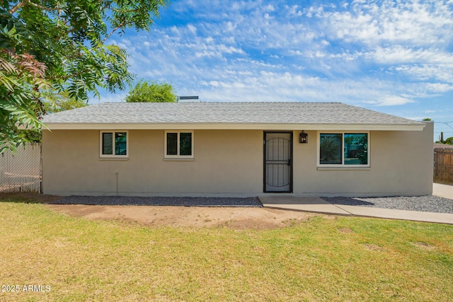 ranch-style home with stucco siding, roof with shingles, fence, and a front yard