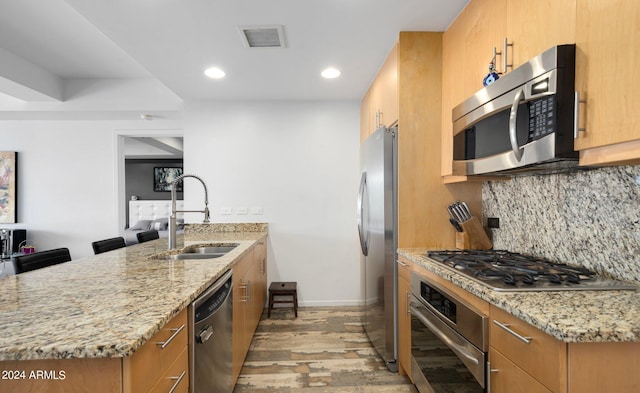 kitchen featuring sink, light hardwood / wood-style flooring, appliances with stainless steel finishes, light stone countertops, and decorative backsplash