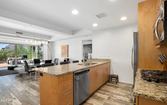 kitchen featuring light stone counters, sink, kitchen peninsula, stainless steel appliances, and light wood-type flooring