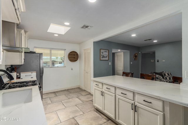 kitchen featuring white cabinetry, light stone counters, white range with gas stovetop, exhaust hood, and a skylight