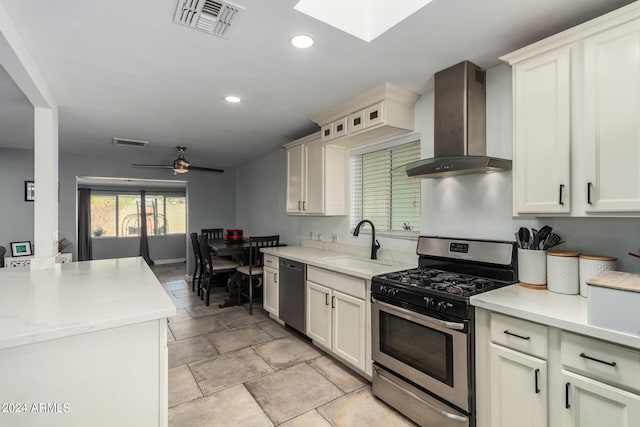 kitchen with wall chimney exhaust hood, stainless steel appliances, ceiling fan, a skylight, and sink