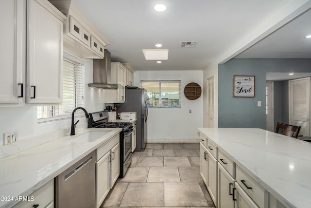 kitchen with light stone counters, sink, wall chimney range hood, appliances with stainless steel finishes, and light tile patterned floors