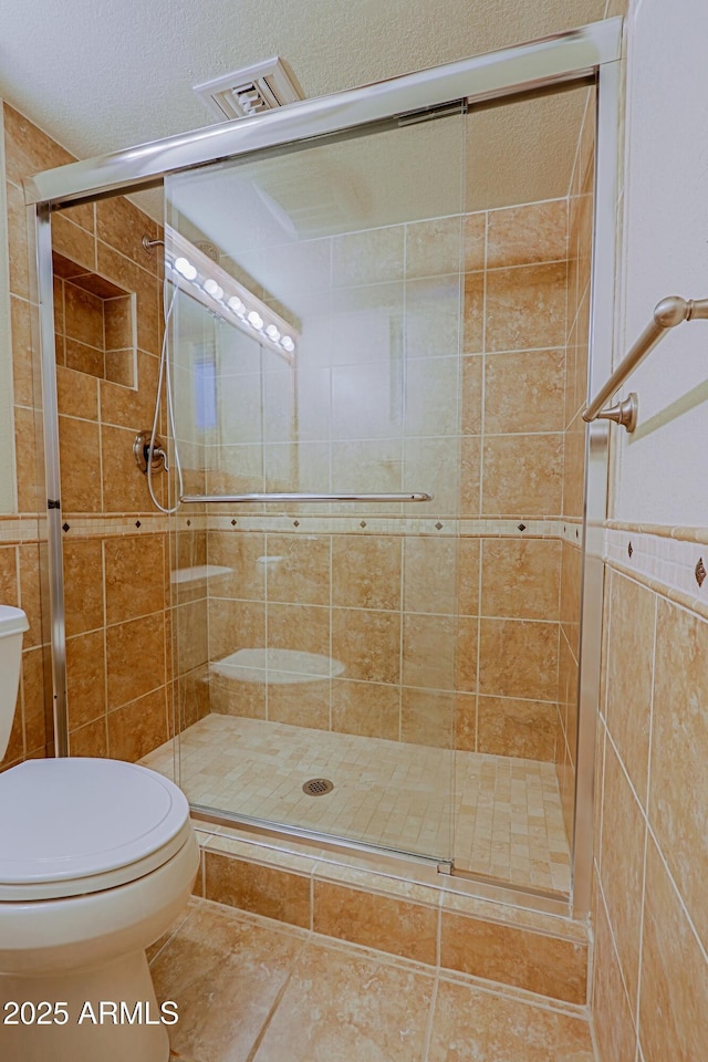 bathroom featuring toilet, a shower with shower door, and tile patterned floors