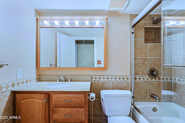 full bathroom featuring tile walls, bath / shower combo with glass door, vanity, and toilet