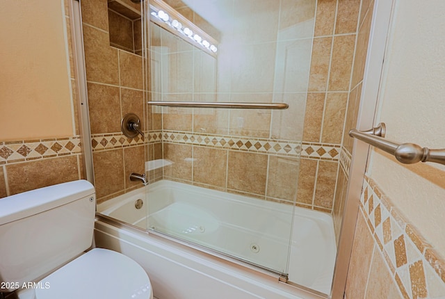 bathroom with tile walls, toilet, and combined bath / shower with glass door