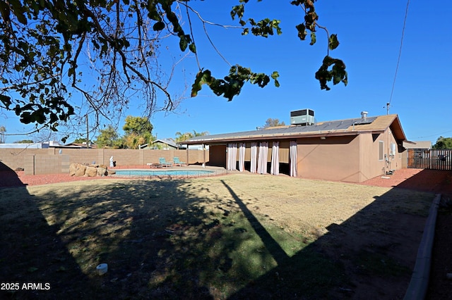 rear view of house with solar panels, cooling unit, and a fenced in pool