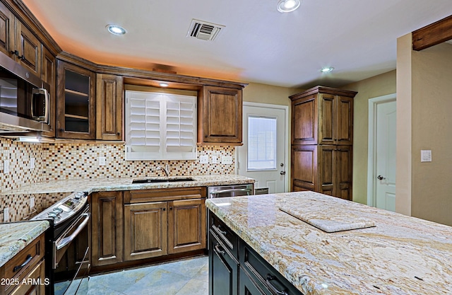 kitchen with sink, stainless steel appliances, backsplash, and light stone countertops