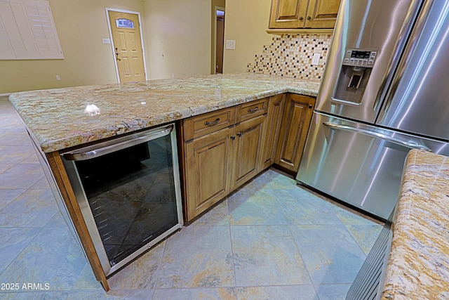 kitchen with wine cooler, stainless steel fridge with ice dispenser, kitchen peninsula, light stone countertops, and backsplash