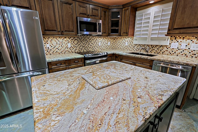 kitchen with sink, stainless steel appliances, light stone counters, and decorative backsplash