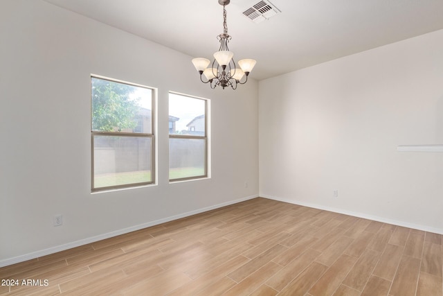 spare room featuring baseboards, light wood-style floors, visible vents, and a chandelier