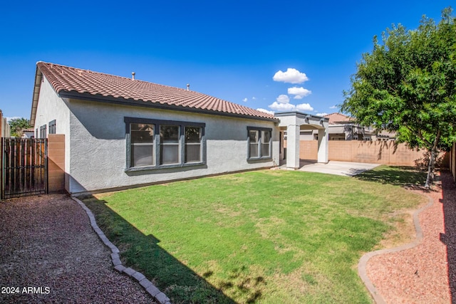 rear view of property with fence, a yard, stucco siding, a tile roof, and a patio area