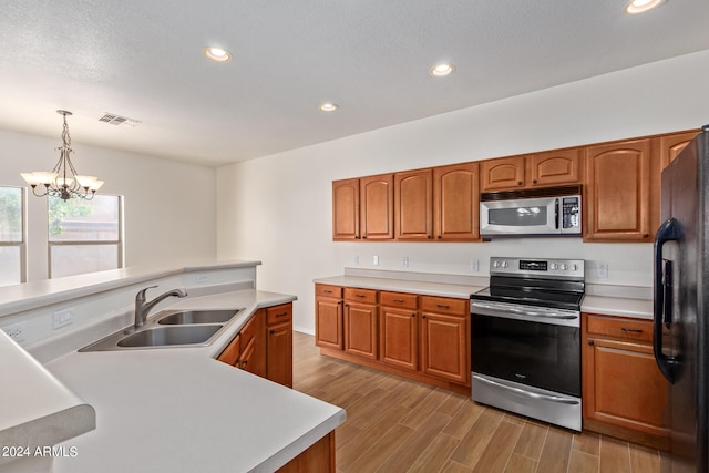 kitchen featuring appliances with stainless steel finishes, pendant lighting, an inviting chandelier, light hardwood / wood-style floors, and sink