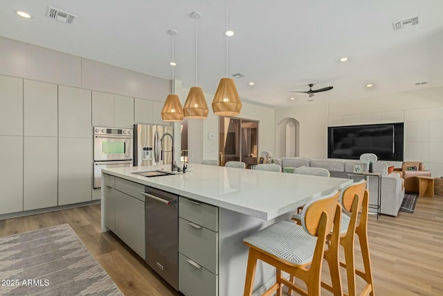 kitchen featuring pendant lighting, sink, stainless steel appliances, light hardwood / wood-style floors, and an island with sink