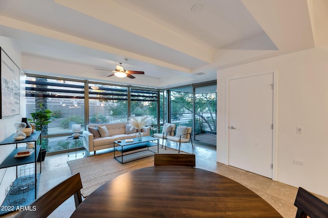 tiled living room featuring ceiling fan, a tray ceiling, a wealth of natural light, and a wall of windows