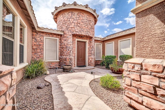 view of exterior entry with stone siding, stucco siding, and a tiled roof