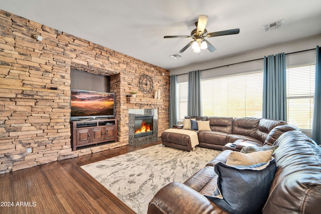 living room with dark wood-style floors, visible vents, a stone fireplace, and a ceiling fan