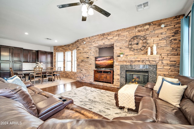 living room with ceiling fan, a stone fireplace, wood finished floors, and visible vents