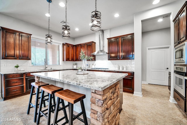 kitchen featuring a kitchen island, a sink, wall chimney range hood, appliances with stainless steel finishes, and backsplash