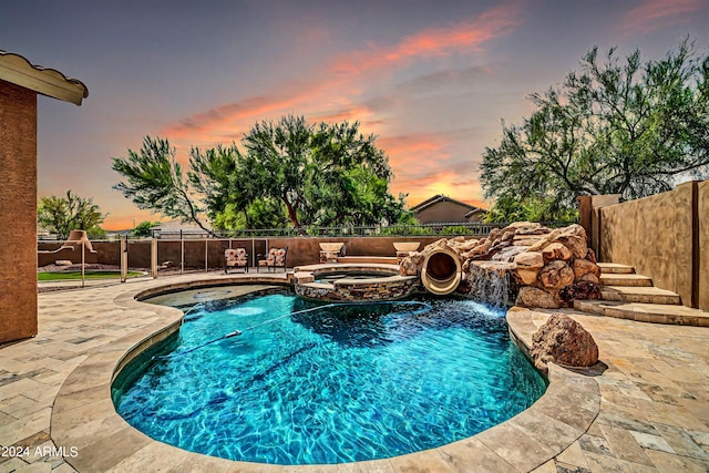 pool at dusk with a pool with connected hot tub, a fenced backyard, and a patio