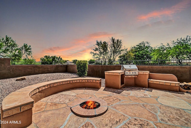 patio terrace at dusk with exterior kitchen, a grill, and fence