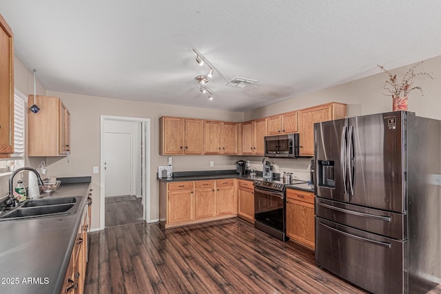kitchen featuring appliances with stainless steel finishes, a sink, dark wood-type flooring, dark countertops, and a textured ceiling