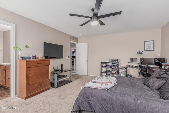 bedroom featuring light carpet, a desk, ensuite bath, and a ceiling fan