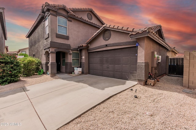 mediterranean / spanish-style home featuring concrete driveway, an attached garage, stucco siding, and fence