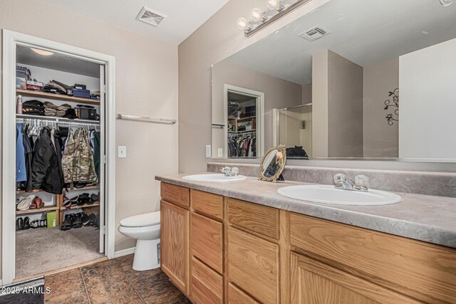 full bathroom with double vanity, a shower with shower door, toilet, and a walk in closet