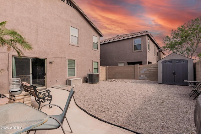 back of house at dusk with a shed, stucco siding, an outbuilding, and a fenced backyard