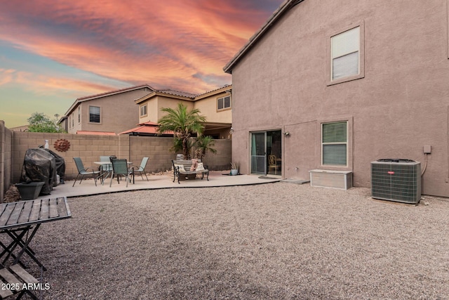 back of property at dusk with central AC, stucco siding, fence, and a patio