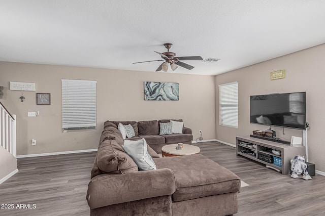 living room featuring wood finished floors, ceiling fan, baseboards, and stairway