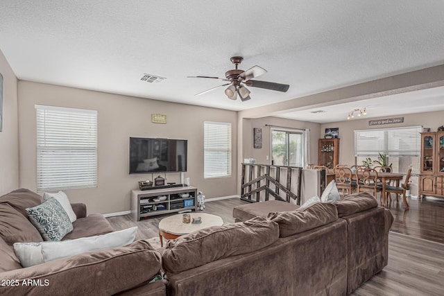 living area featuring ceiling fan, wood finished floors, baseboards, and a textured ceiling