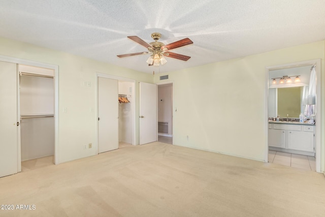 unfurnished bedroom featuring connected bathroom, ceiling fan, light carpet, and two closets