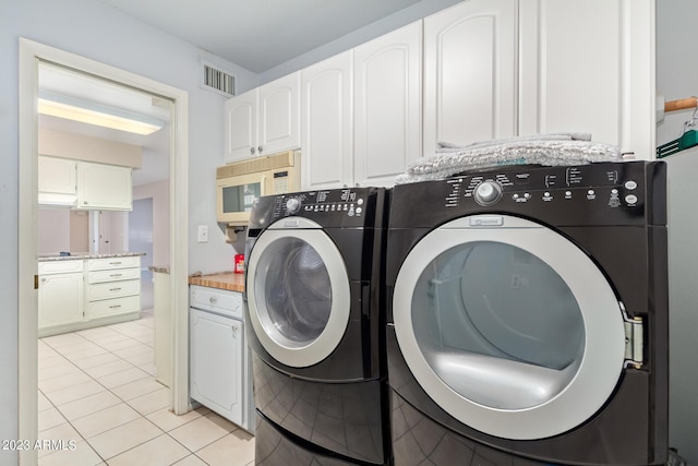 clothes washing area with separate washer and dryer, light tile patterned floors, and cabinets